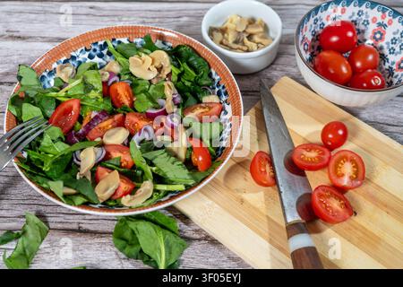 Healthy vegan meal in a bowl, featuring fresh spinach, tomatoes, mushrooms, red onion, on a rustic wooden table Stock Photo