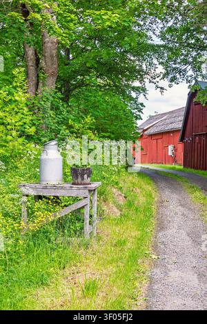 Milk can on a stand by a road at a red barn Stock Photo