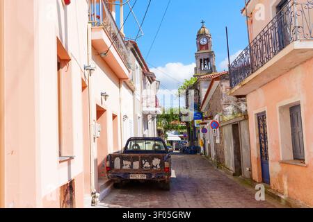 Lesbos, Greece - April 23, 2026: Narrow cobblestone street in Mantamados on Lesbos Island features charming pastel-colored houses, an old parked picku Stock Photo
