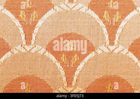 Horizontal close up macro shot of an orange and beige upholstery fabric texture featuring an embroidered vintage geometric scale or floral damask styl Stock Photo