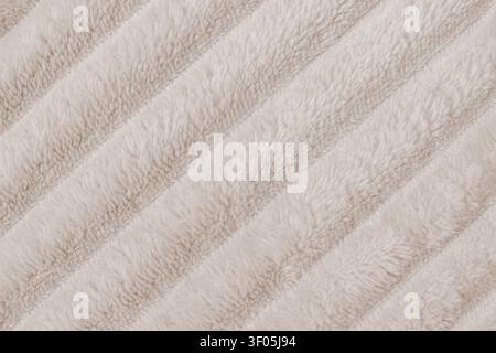 Horizontal close up flat lay shot of a cozy beige plush fleece blanket fabric texture with distinct diagonal ribbed rows of soft fluffy synthetic fur Stock Photo