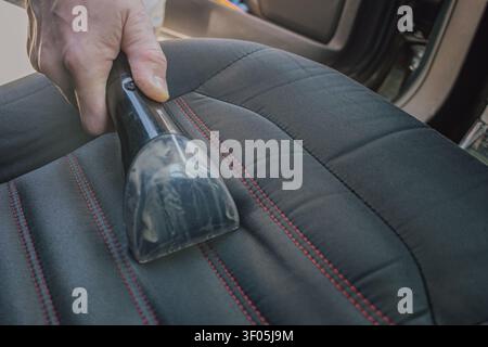 Horizontal close up shot of a man cleaning a black fabric car seat upholstery with red stitching details using a professional vacuum water extraction Stock Photo