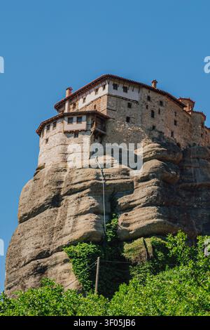 Vertical close up shot of a historic stone orthodox monastery building standing on a high sandstone cliff edge with green climbing ivy on a bright sun Stock Photo