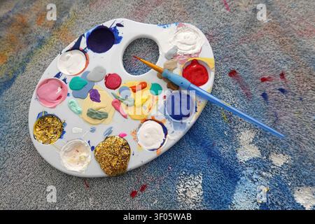 A plastic artist's palette with a variety of paint colors, including pink, white, red, blue, yellow, and gold glitter. Stock Photo
