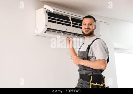 Technician repairing wall-mounted air conditioner indoors Stock Photo