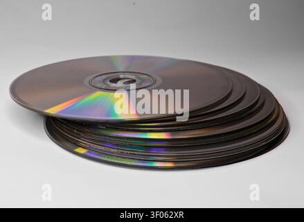 Stack of CDs and DVDs on a clean white surface, showing reflective optical media, data storage, and outdated technology concepts. Stock Photo