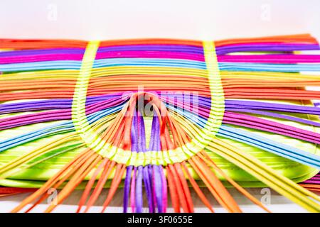 Close up of colorful handmade woven purse with vibrant rainbow ribbons and abstract pattern on white background Stock Photo