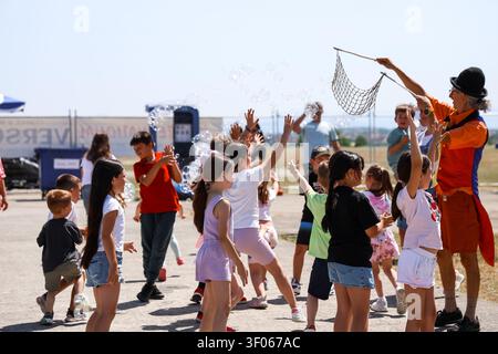 A costumed entertainer creates giant soap bubbles for a joyful crowd of children reaching up and playing outdoors on a sunny day. Stock Photo