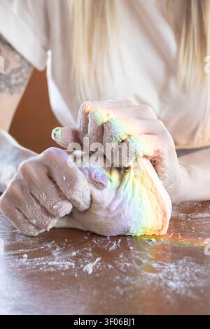 Close-up of flour-dusted hands kneading homemade sourdough bread dough on a wooden table, showcasing artisan baking, texture, and craft in a warm kitc Stock Photo