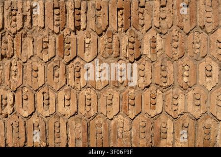 Close-up of an old clay brick wall with repeating geometric relief blocks, showing weathered surface, earthy tones, rough texture, and strong symmetry Stock Photo