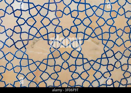 Traditional Islamic geometric tessellation with interlaced blue lines on a beige stone surface, forming repeating stars and polygons for elegant archi Stock Photo