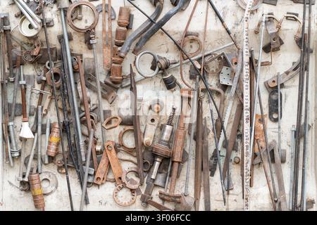 Assorted rusty metal tools, rods, brackets and rings arranged on a weathered workshop wall, creating an industrial background with textures of wear, r Stock Photo