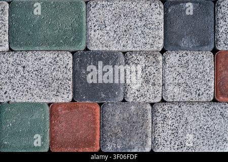 Detailed close-up of granite cobblestone pavement in gray, green, and red tones, showing rough stone texture and rectangular paver pattern for urban b Stock Photo