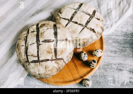 Two rustic artisan bread loaves on a wooden board with scattered quail eggs, styled for authentic cooking, organic ingredients, and homemade bakery tr Stock Photo