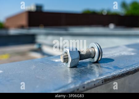 Photos of a galvanized hex nut, bolt, and flat washer assembly is resting on a silver steel beam, industrial metal surface outdoors. Stock Photo