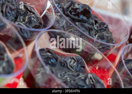 Close-up of dark berry dessert topping in individual plastic cups, creating a festive catering buffet detail with glossy fruit texture, soft focus and Stock Photo