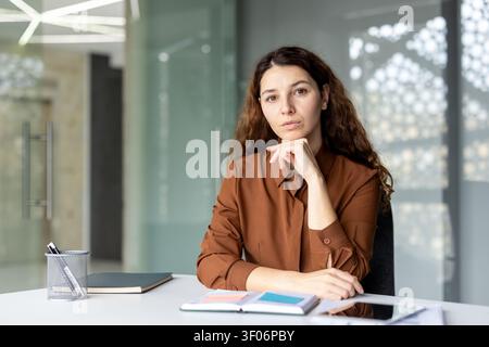 Serious businesswoman sitting at a desk with a pensive expression. Considering business plans and future development in a minimalist corporate environment Stock Photo