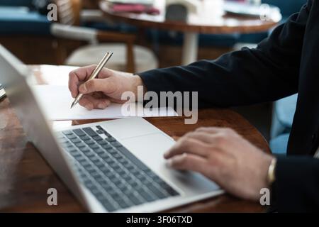 Businessman writing notes while working on laptop Stock Photo
