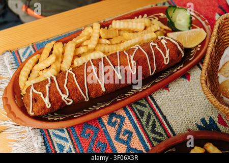 Traditional Karadjordjeva schnitzel served with crispy French fries, cucumber and lemon. A classic Balkan dish presented on a rustic ceramic platter. Stock Photo