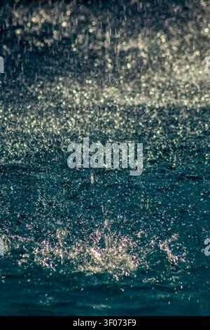 Close-up of intense rain drops falling and creating splashes on a deep blue water surface during a tropical storm in Brazil. Perfect for concepts Stock Photo