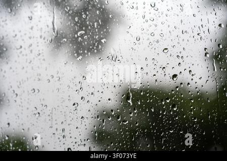 A close-up, atmospheric shot of water droplets on a window pane, creating a soft-focus, blurred background. This image captures a rainy, melancholic w Stock Photo