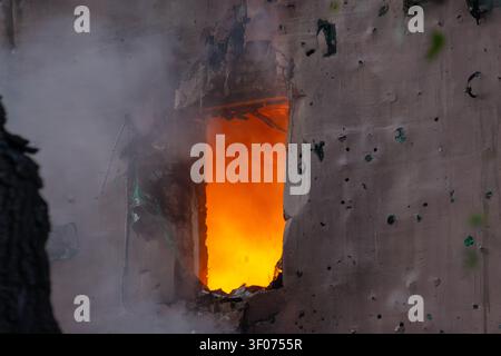 Intense flames blazing through a shattered window of a heavily damaged structure Stock Photo