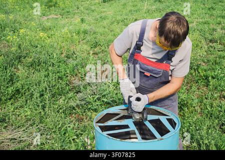 Worker using an angle grinder to cut metal barrel for DIY upcycling project Stock Photo