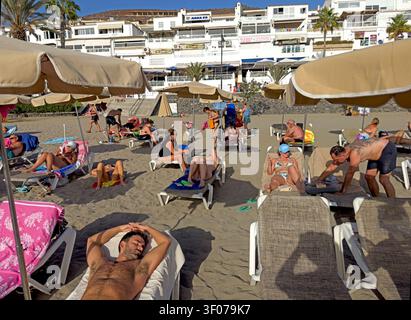 Northern European and Russian holidaymakers crowd the dark-sand beach at Los Cristianos, Tenerife, during a winter-sun break. Stock Photo