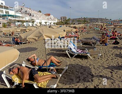 Northern European and Russian holidaymakers crowd the dark-sand beach at Los Cristianos, Tenerife, during a winter-sun break. Stock Photo