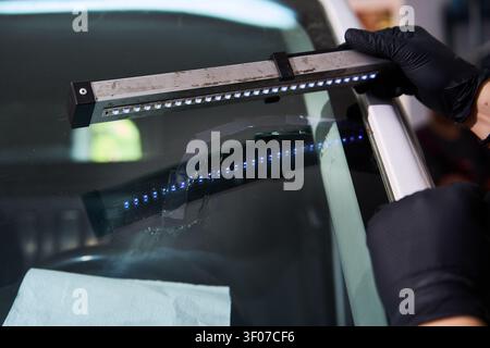 Windshield UV Resin Curing. Windshield repair. Automotive technician holds ultraviolet lamp over broken car glass. Mechanic cures resin inside windshi Stock Photo