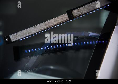Mechanic cures resin inside windshield crack using lighting equipment. Windshield UV Resin Curing. Windshield repair. Automotive technician holds ultr Stock Photo