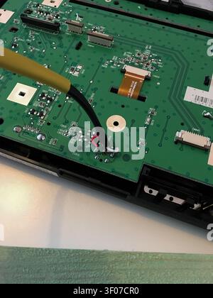 Green circuit board of a car radio with a soldering iron and ribbon cable during repair. Stock Photo