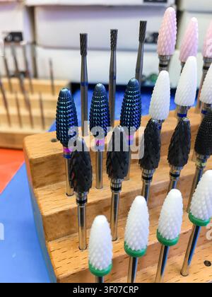 Set of nail drill bits standing on a wooden holder on a blue mat. Stock Photo