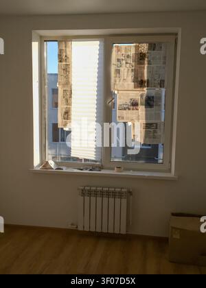 Empty room with a window covered by blinds and a radiator on the wall with wooden floor. Stock Photo