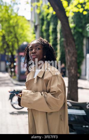 Curious african american woman lurking waiting for taxi while standing on city street holding phone. Stock Photo
