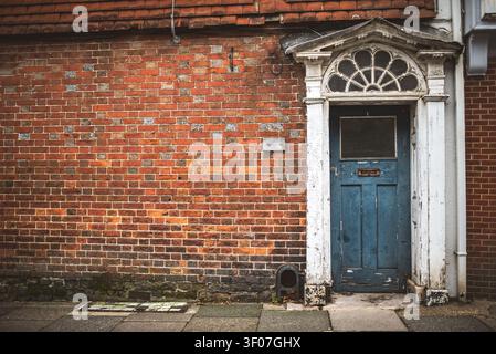 A charming, aged blue wooden door with a mail slot and a decorative fanlight above, nestled within a textured brick facade Stock Photo