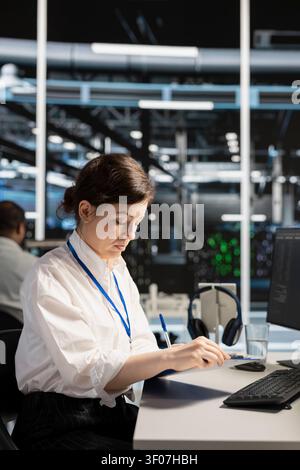 Server room worker reviews performance analytics on a clipboard in a data center to optimize storage systems and resource use. Stock Photo