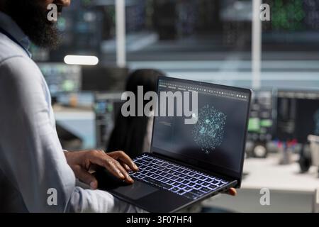 Data center engineer uses a laptop computer in a data center to manage AI virtualization and optimize server infrastructure. Stock Photo