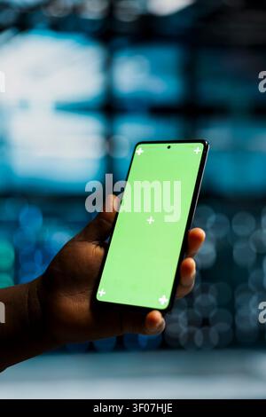 Data center engineer works with a chroma key smartphone, using an editable screen to review performance data. Stock Photo
