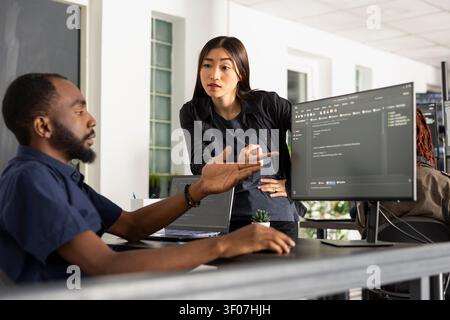 Multiethnic programmers analyzing HTML scripts on desktop monitor and laptop, working on web project. Team collaboration highlights communication, problem solving and modern app development strategy. Stock Photo