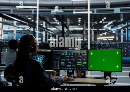 IT specialist uses a green screen computer in a data center for server operations, screen replacement, and server workflow monitoring. Stock Photo