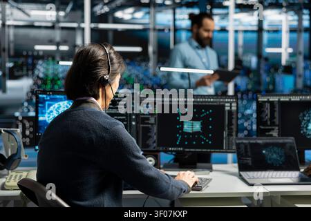 Administrator wears a headset in a server hub, using artificial intelligence troubleshooting to assist users. Stock Photo