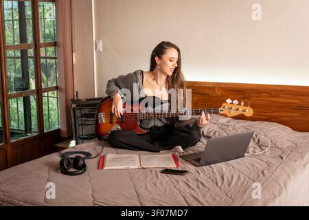 Female Bass Guitar Student Studying Music Remotely at Home Stock Photo