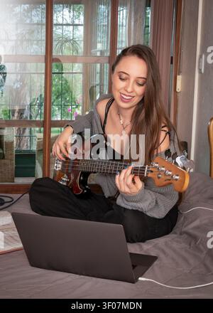 Young woman learning bass guitar during an online music lesson at home Stock Photo