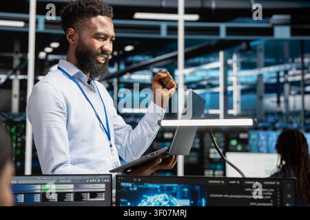 Pleased data center administrator celebrates after configuring machine learning systems with AI technology in a data center. Stock Photo