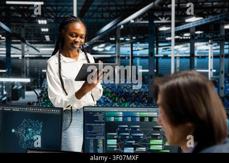 Cheerful server facility software engineer working with digital tablet, coding, supervising systems for uptime and efficiency. Stock Photo