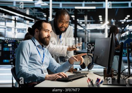 Team of system administrators working with workstation in server environment, analyzing data. Stock Photo