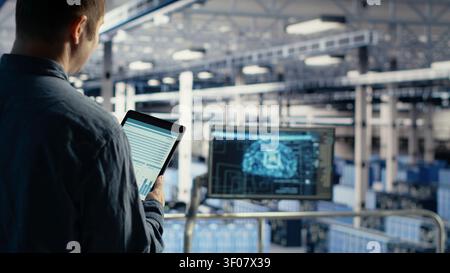 IT expert uses a tablet touchscreen in a server room to review data charts and monitor equipment health. Stock Photo