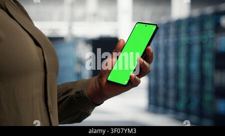 Server facility software engineer works with green screen mobile mobile device to watch video tutorial on how to update rig. Stock Photo