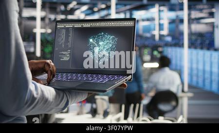 Data infrastructure center system admin working with machine learning algorithms on notebook to assess large datasets, while working with AI on notebook to recognize data patterns. Stock Photo